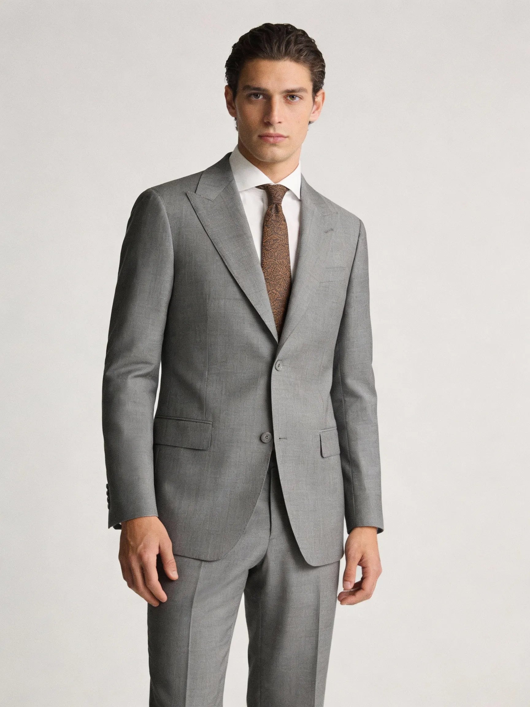 Man wearing a gray suit with a white shirt and brown tie on a light gray online sale blazer and suits