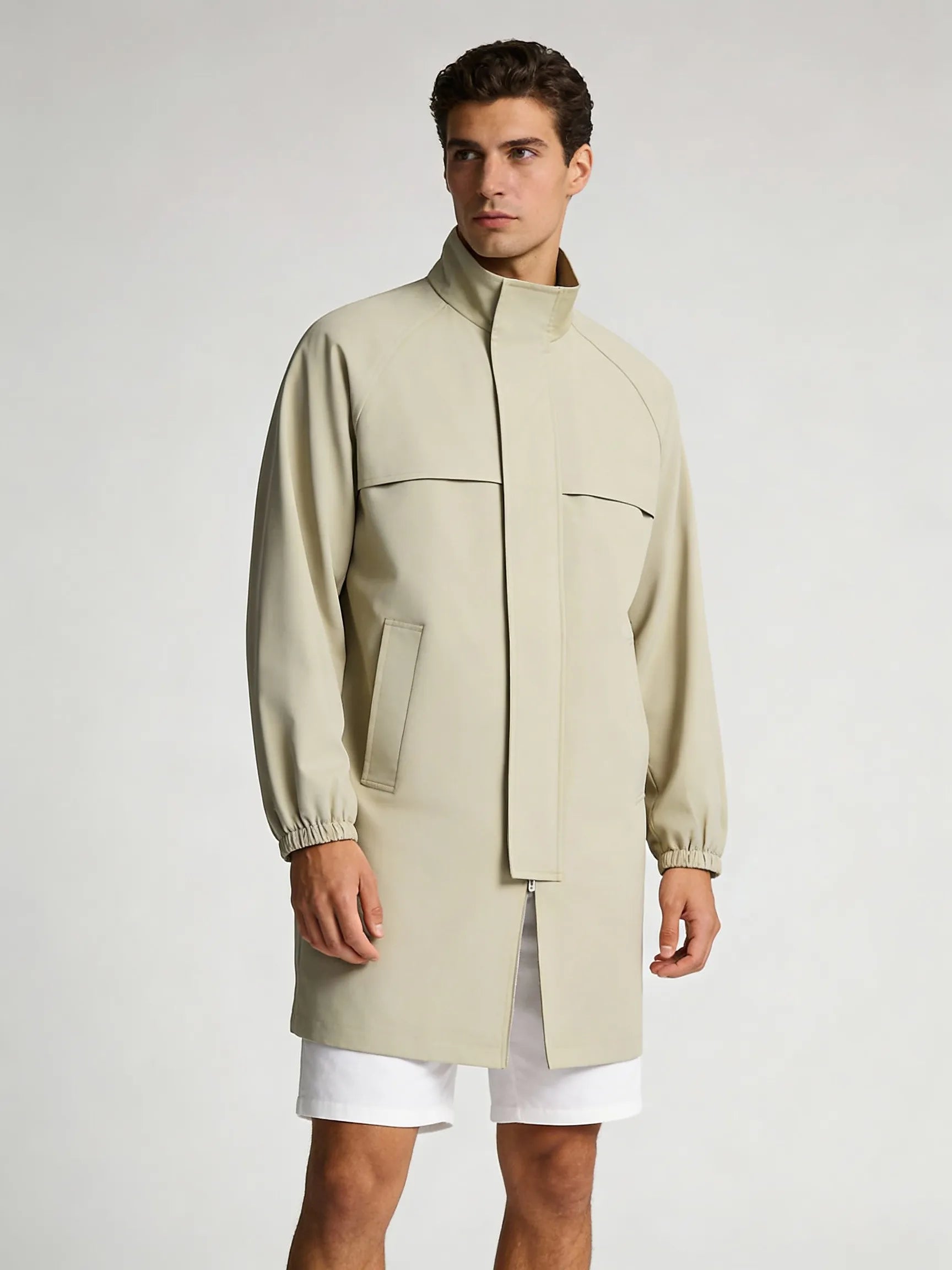 Man wearing a beige trench coat over white shorts on a light gray golf background