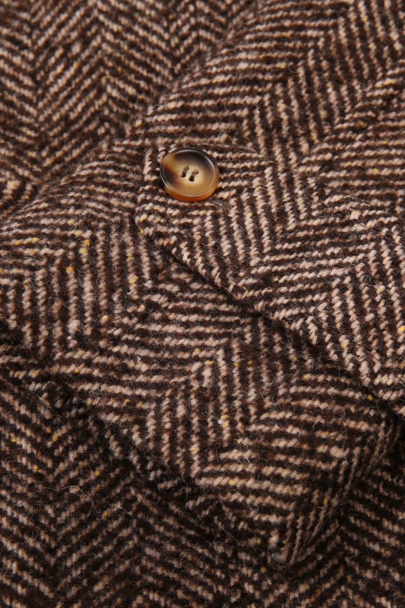 Close-up of a brown herringbone patterned fabric with a button. tweed custom made suits and jackets 